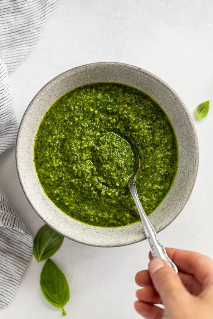 Bowl of pesto with hand taking a spoonful.