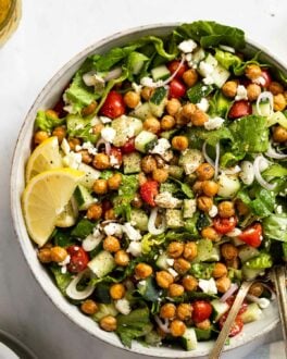 Up close bowl of Greek salad with crispy chickpeas, lemon wedges, with a spoon.