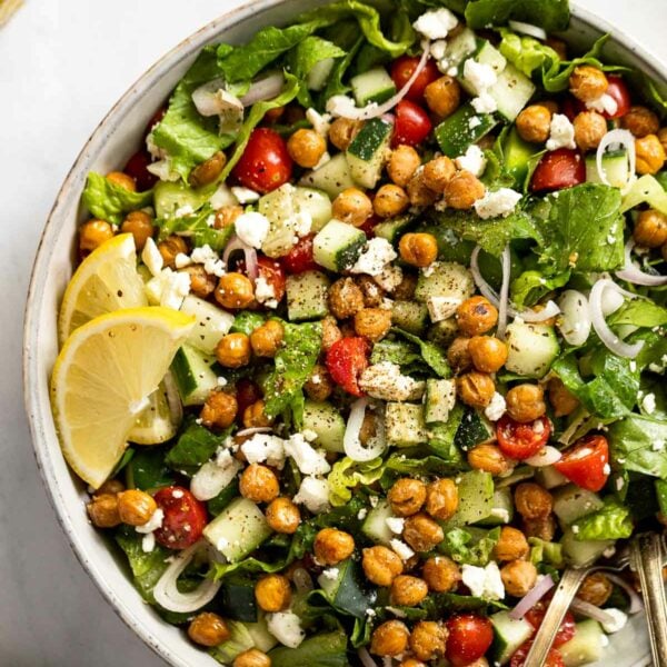Up close bowl of Greek salad with crispy chickpeas, lemon wedges, with a spoon.