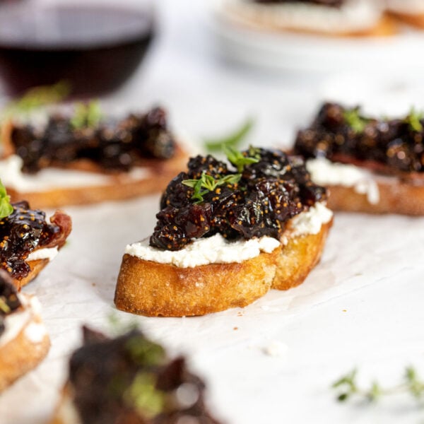 Fig compote and goat cheese crostini next to wine glasses.