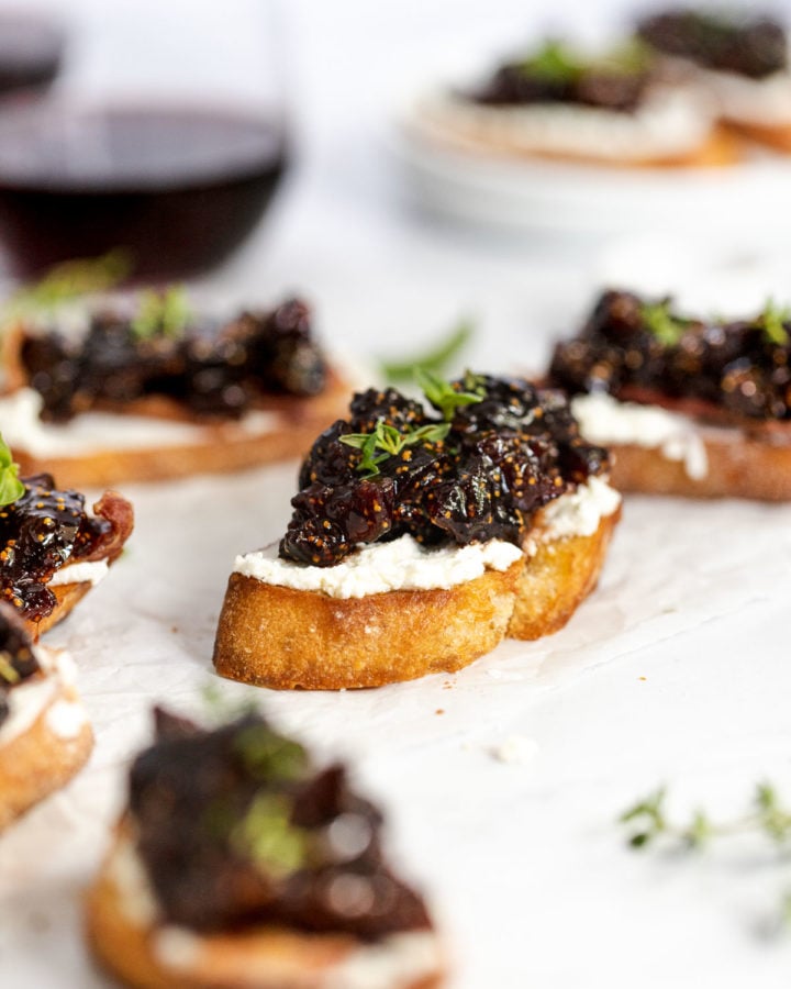 Fig compote and goat cheese crostini next to wine glasses.