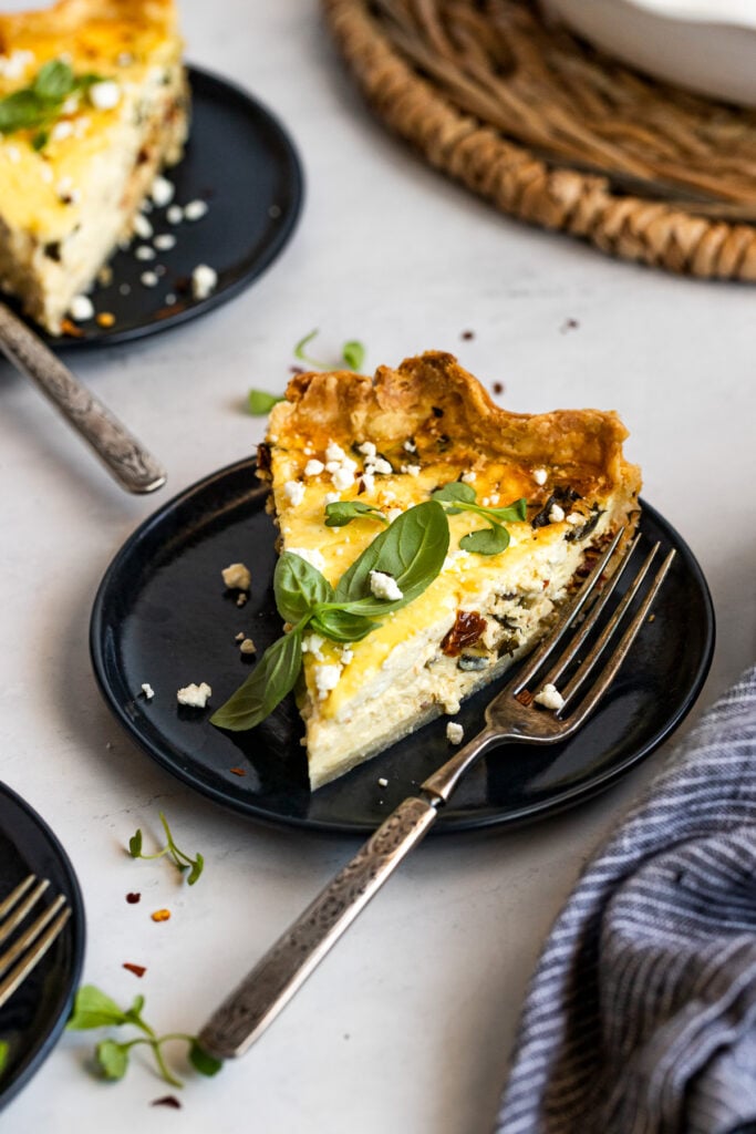 Slice of mediterranean quiche on plate with fork garnished with basil.