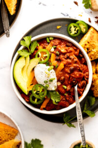 Bowl of vegetarian bean chili with spoon and toppings.