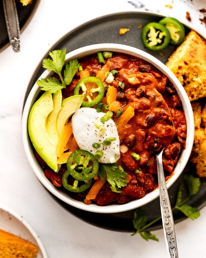 Bowl of vegetarian bean chili with spoon and toppings.