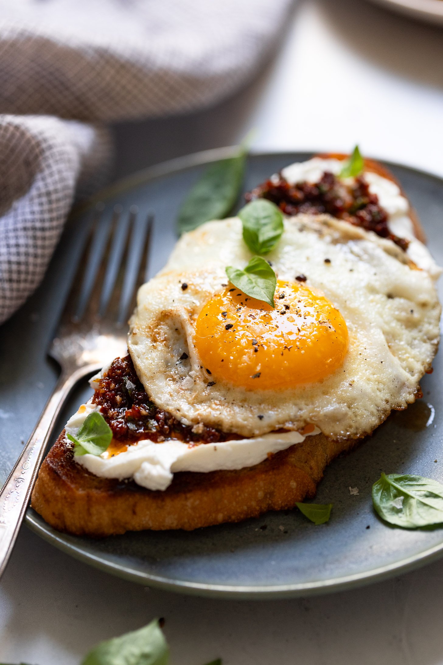 Plate with goat cheese toast topped with fried egg and basil leaves.