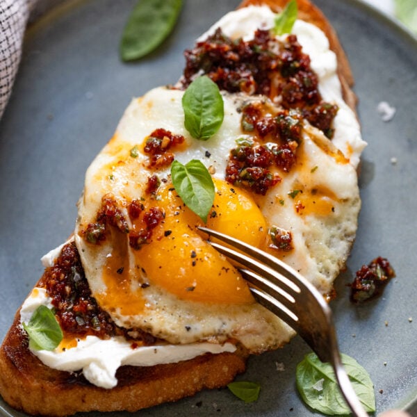Toast with goat cheese, sun-dried tomatoes, and fried egg with fork.