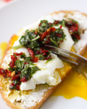 Goat cheese toast with poached egg and fork breaking into it with basil mixture on top.