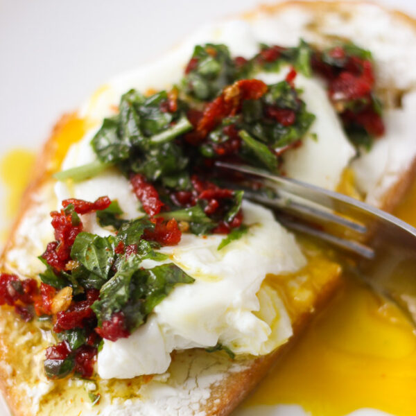 Goat cheese toast with poached egg and fork breaking into it with basil mixture on top.