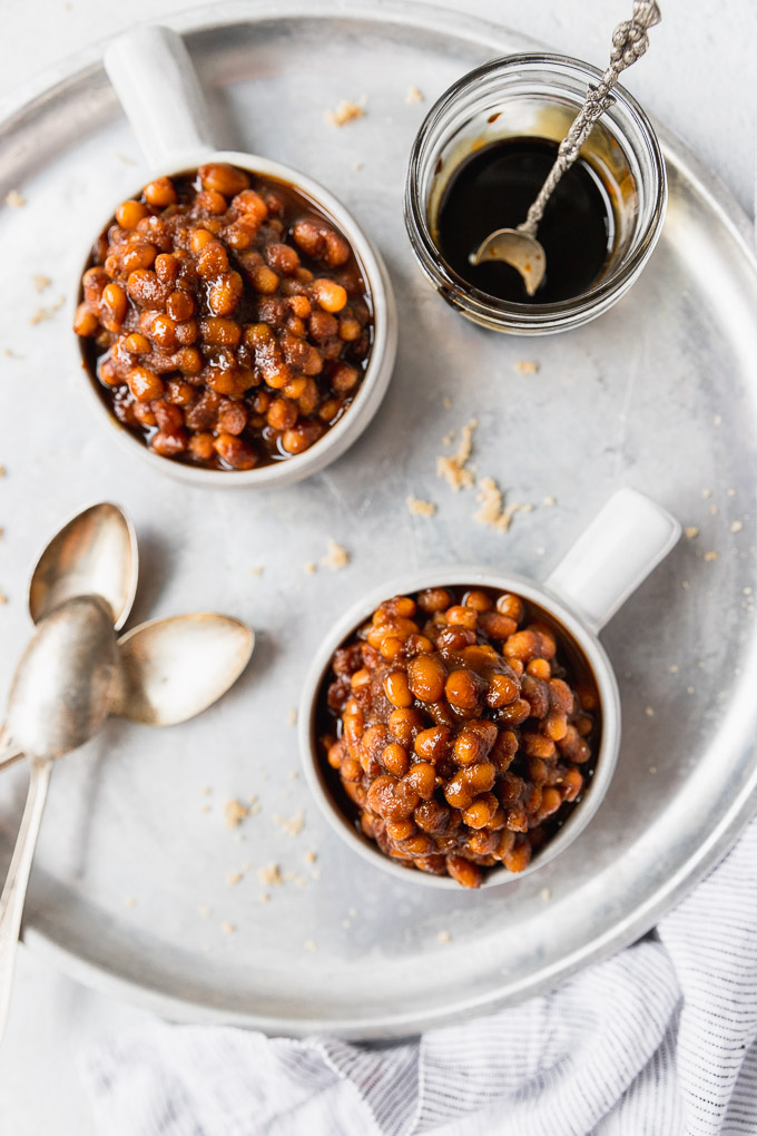 Two small bowls of beans next to molasses and spoons.