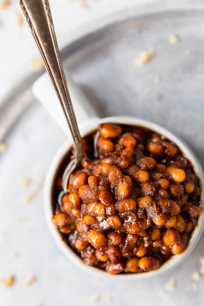 Baked beans in small bowl with spoon on tray.