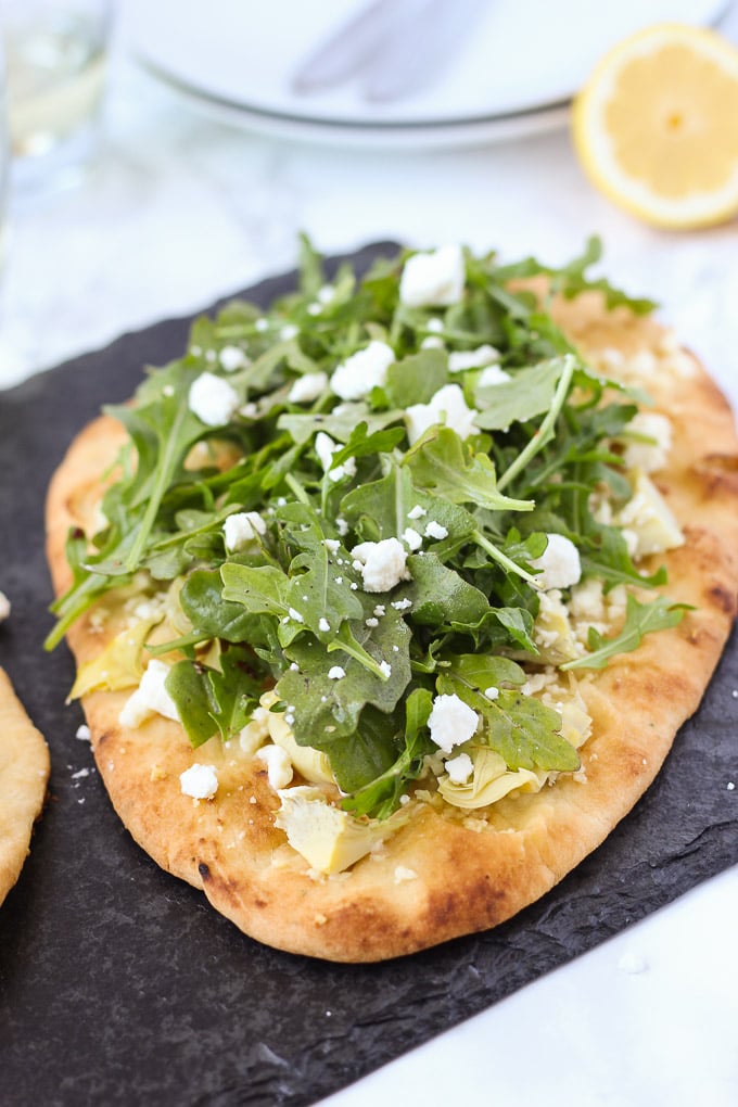 naan flatbread topped with artichokes and arugula on black slate