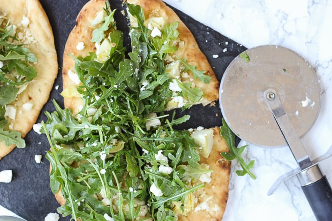 cut pieces of naan Artichoke and Arugula Flatbread with pizza cutter on black slate