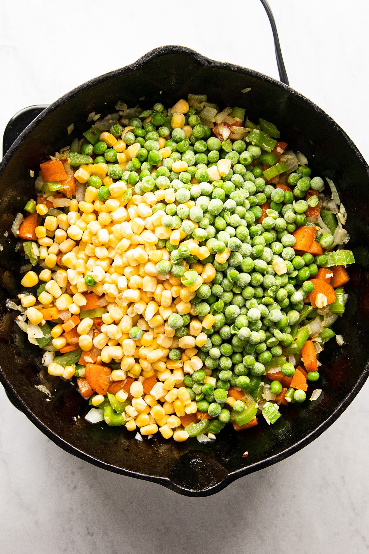 Skillet with frozen corn and peas added.