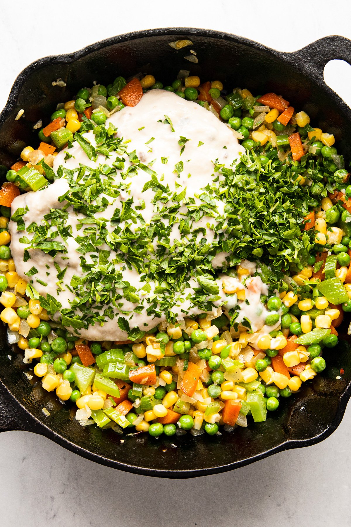 Skillet with vegetables topped with cream of mushroom soup and chopped parsley.