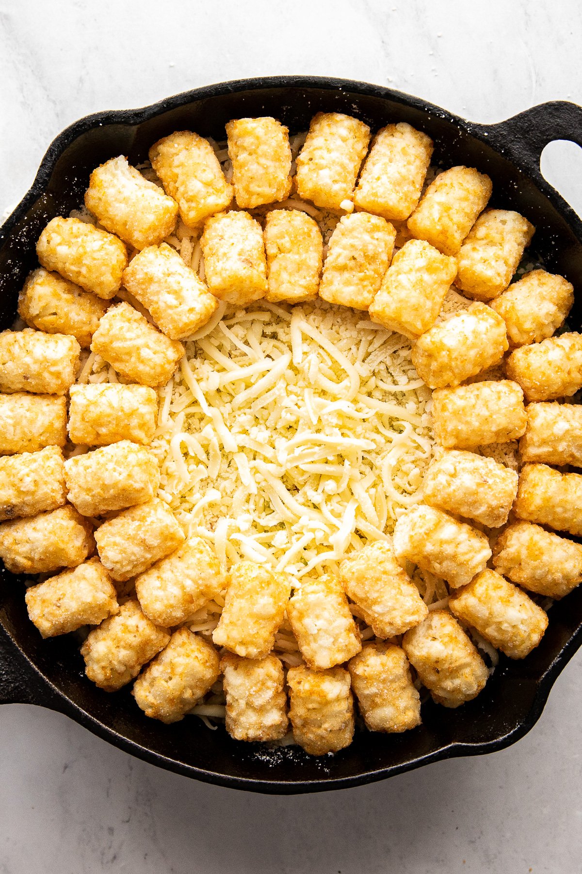 Tater tots in second circle around hotdish in skillet.