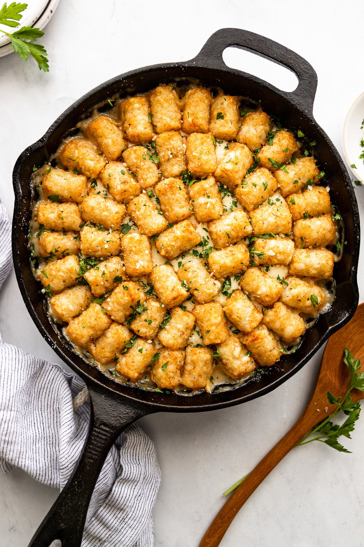 Tater Tot hotdish in cast iron skillet after baking next to serving spoon.
