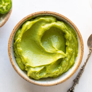 Avocado sauce in small bowl next to spoon.