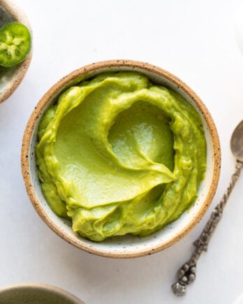 Avocado sauce in small bowl next to spoon.