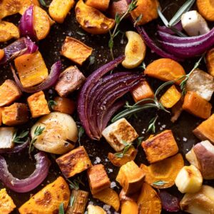 Baking sheet with roasted root vegetables: onion, garlic, sweet potato, carrot, parsnip.