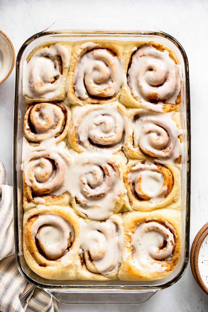 Cinnamon rolls in pan next to icing and plates.