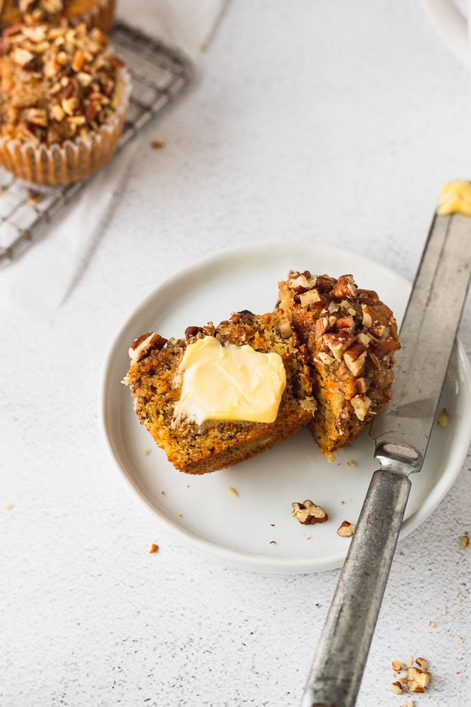 banana carrot muffin cut in half on white plate with butter and knife next to it