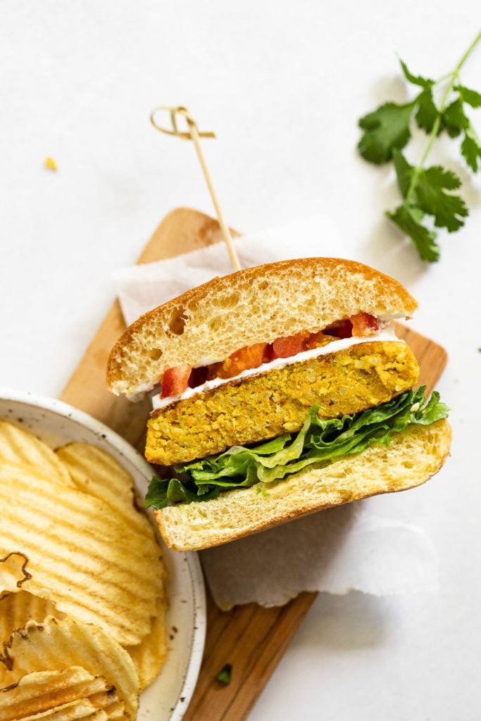 Curried Chickpea Burger cut in half on its side on a tray next to potato chips.