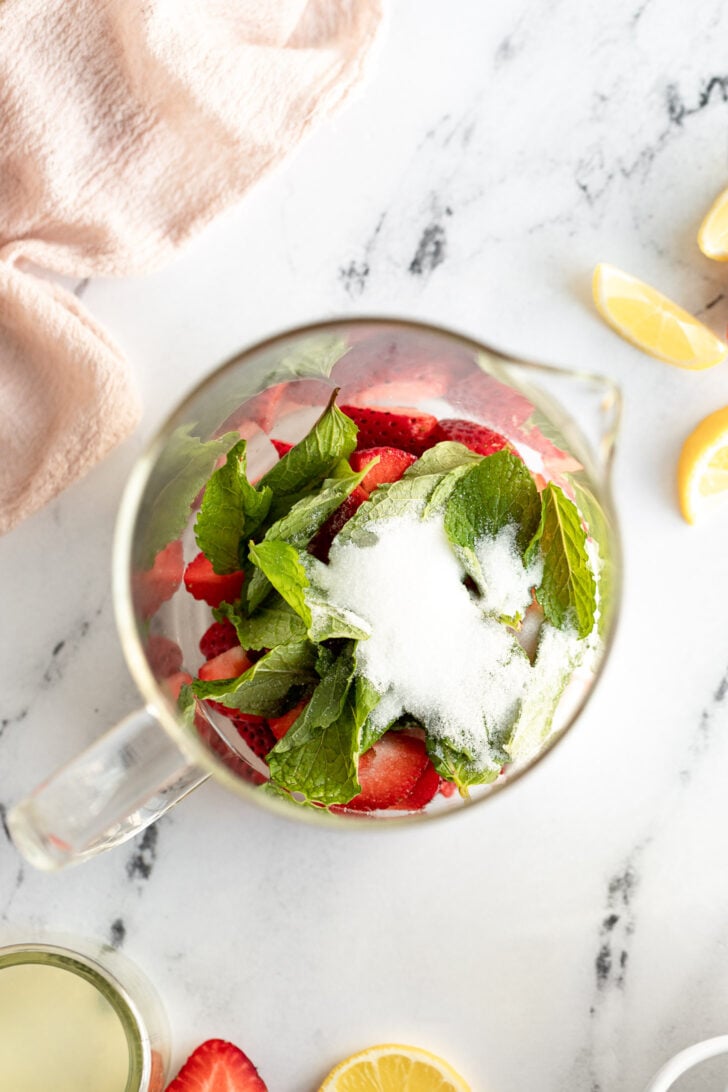 Strawberries, mint, and sugar in pitcher.