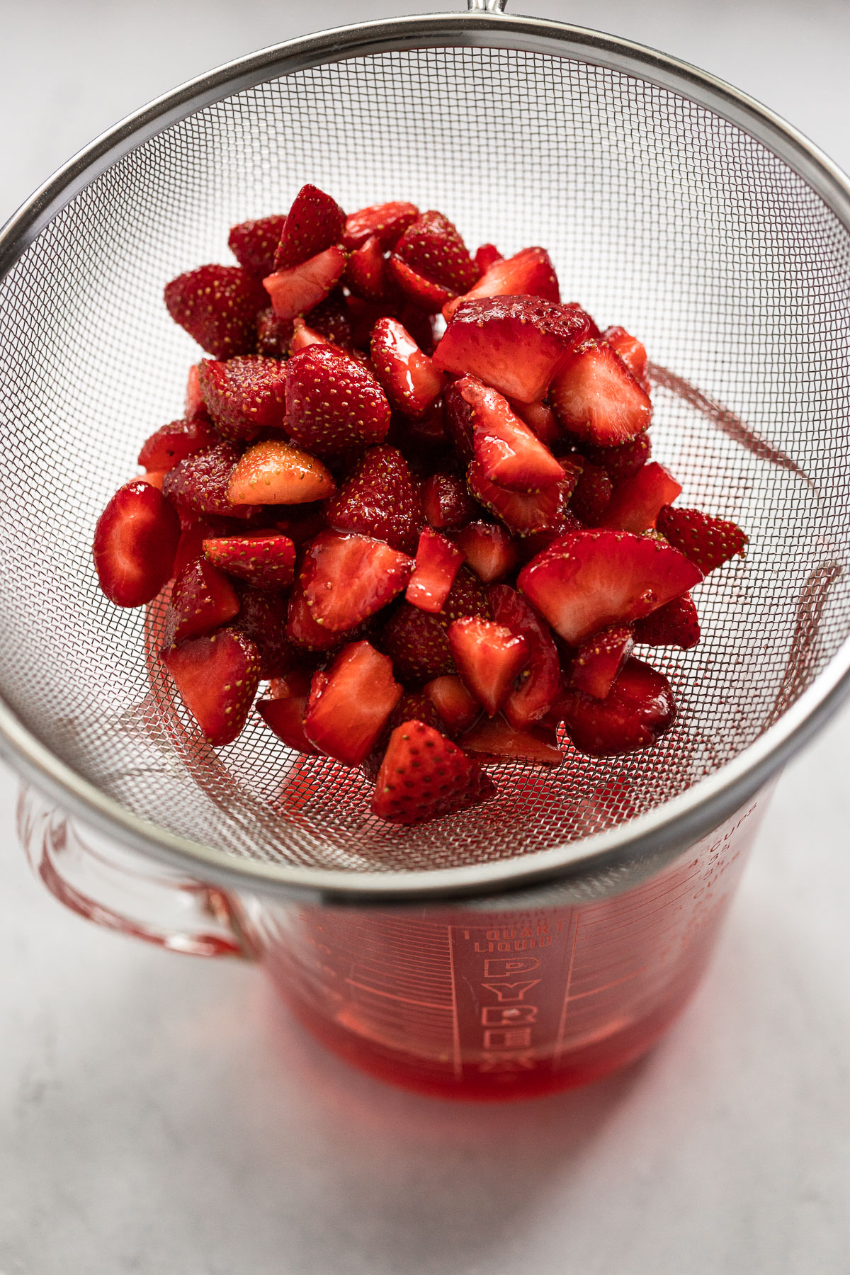 Strawberries straining juice in measuring cup.