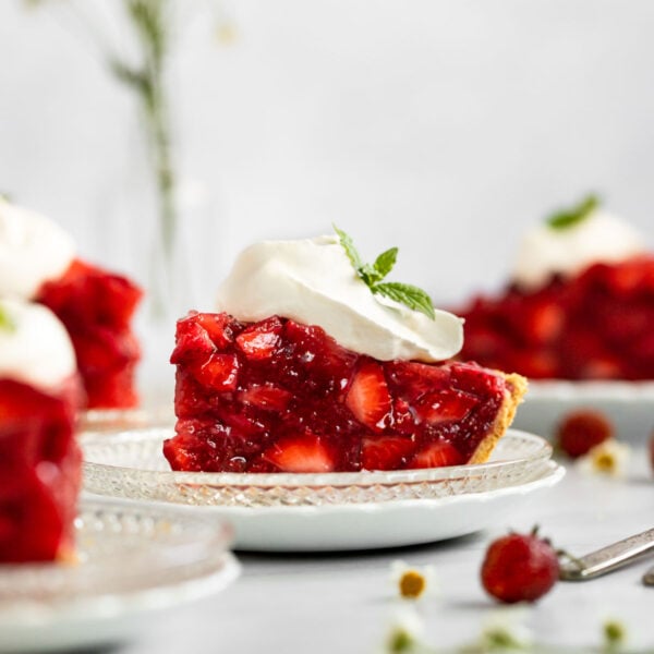 Slice of strawberry pie with whipped cream on plate next to other slices.