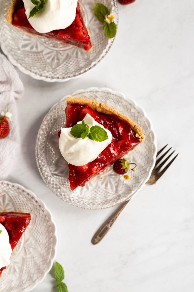 Overhead strawberry pie slice next to two other plates and a fork.