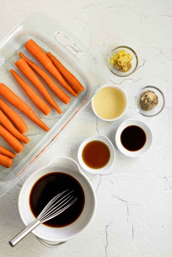 Carrots in dish next to soy sauce and small bowls of ingredients.