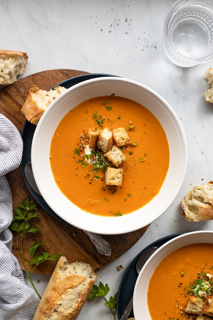 Two bowls of tomato carrot soup with croutons.
