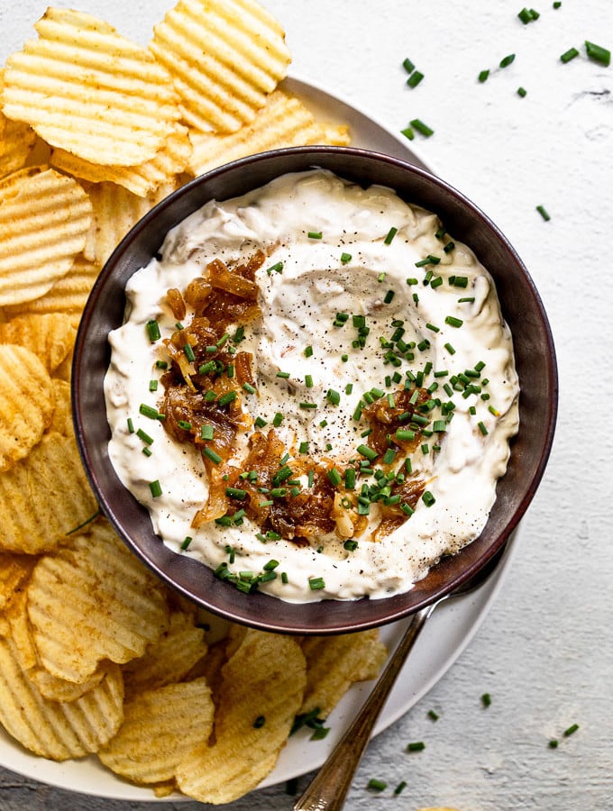 Bowl of onion dip with caramelized onion topping and chives next to chips.