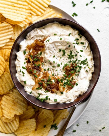 Bowl of onion dip with caramelized onion topping and chives next to chips.