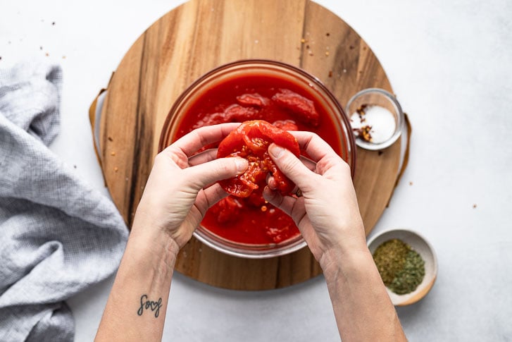 Hand holding peeled whole tomato over bowl.