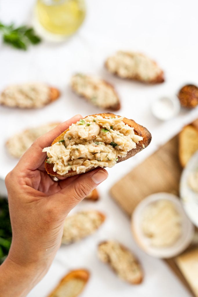 Hand holding crostini with white bean mixture spread on it.