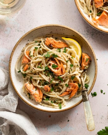 Bowl of pasta with pieces of salmon and lemon wedge.