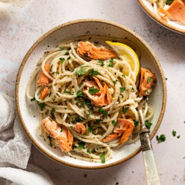 Bowl of pasta with pieces of salmon and lemon wedge.