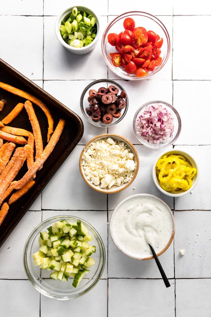 Bowls of toppings next to pan of fries.