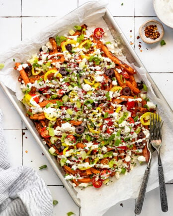 Sheet pan with loaded sweet potato fries with tzatziki bowl and forks.