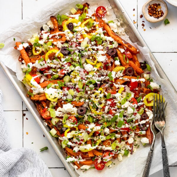 Sheet pan with loaded sweet potato fries with tzatziki bowl and forks.