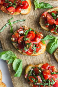 Overhead looking at bruschetta on cutting board next to basil leaves.