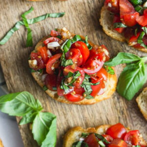 Overhead looking at bruschetta on cutting board next to basil leaves.
