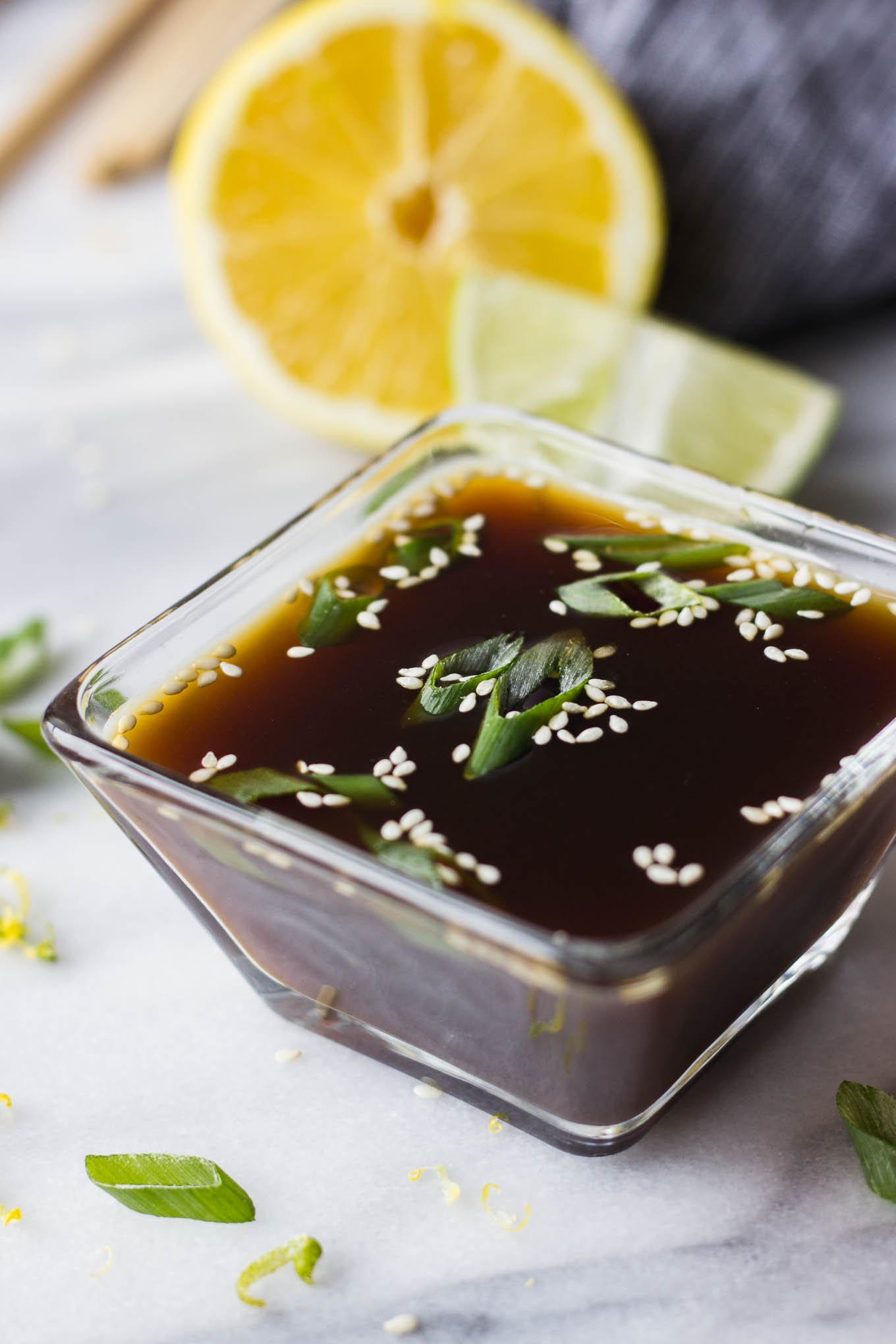 Ponzu sauce in glass dipping bowl garnished with green onion and sesame seeds.