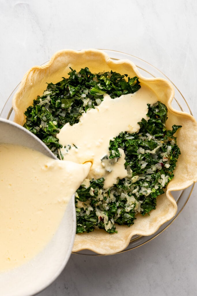 Egg mixture pouring into pie crust over kale.