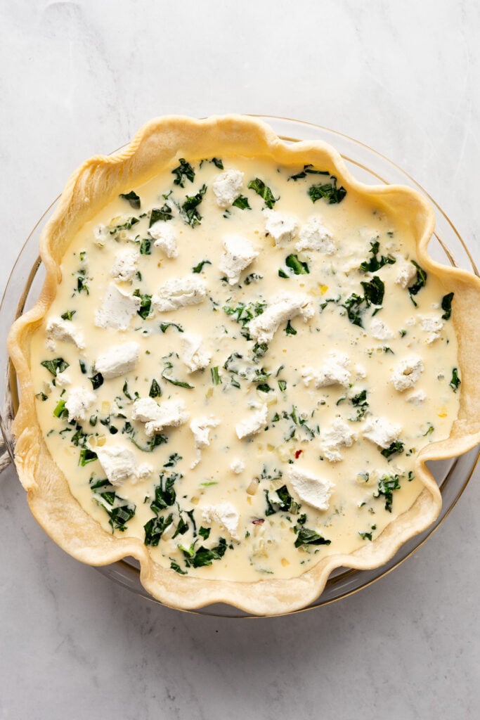 Goat cheese dotted on top of quiche before baking.
