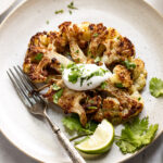 Oven roasted cauliflower steak with seasoning topped with sour cream and cilantro on plate.