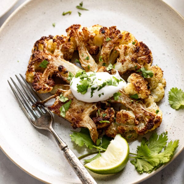 Oven roasted cauliflower steak with seasoning topped with sour cream and cilantro on plate.