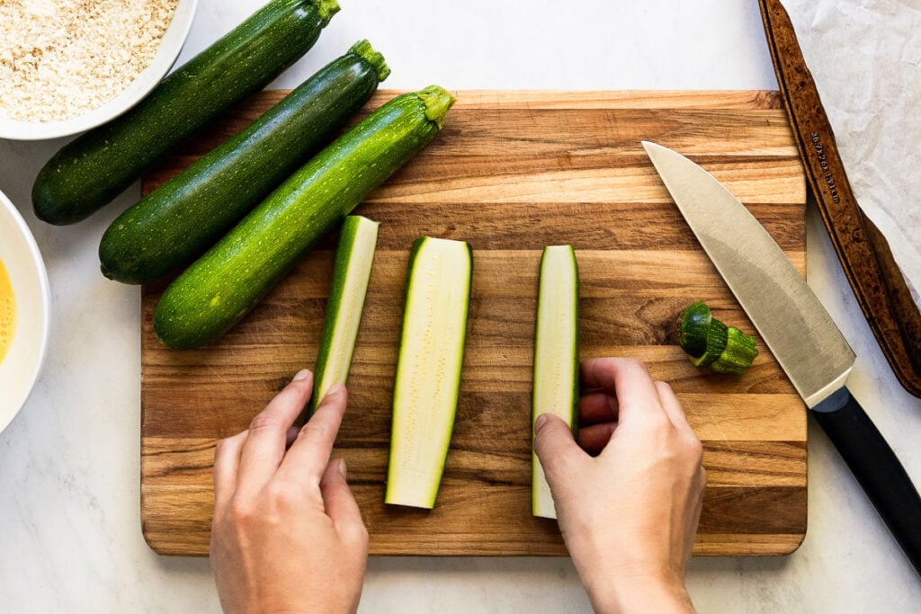 Zucchini cut into planks on cutting board with hands holding two.