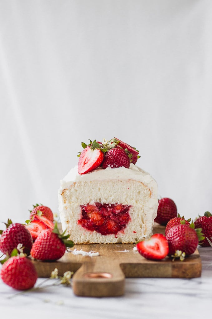 Inside look of strawberries inside angel food cake garnished with more strawberries on wood tray.